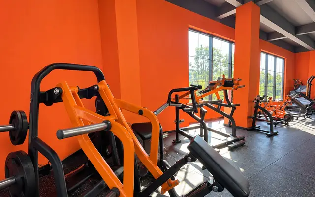 Strength gym with orange-framed machines and large windows