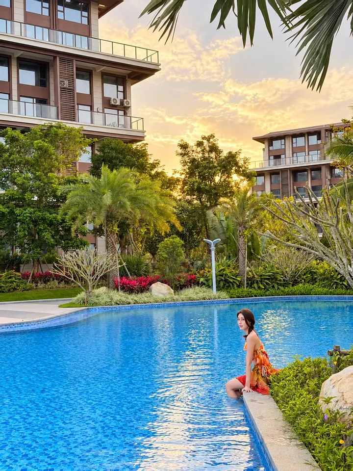 Guest sitting at the edge of a pool below palm trees and apartment buildings at sunset